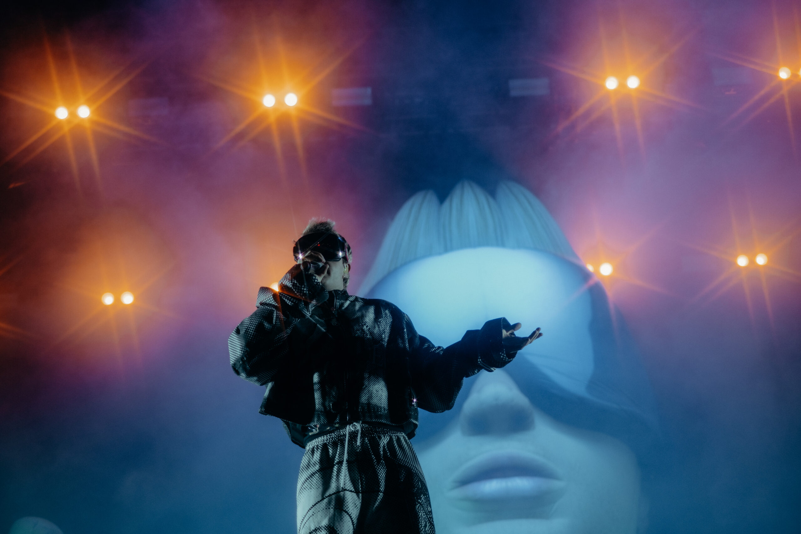 Der Künstler Ski Aggu auf der Bühne beim Heroes Festival 2025, eingefangen in einem intensiven Moment mit Lichtshow in Blau und Orange. Fotografiert von Pia Oechsner – Konzertfotografie mit Fokus auf Emotion und Atmosphäre.